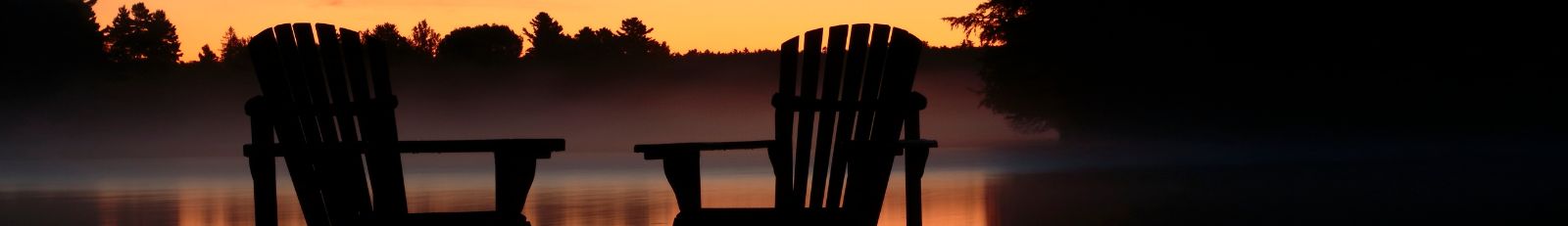 Image of two lawn chairs sitting at end of dock on a lake.
