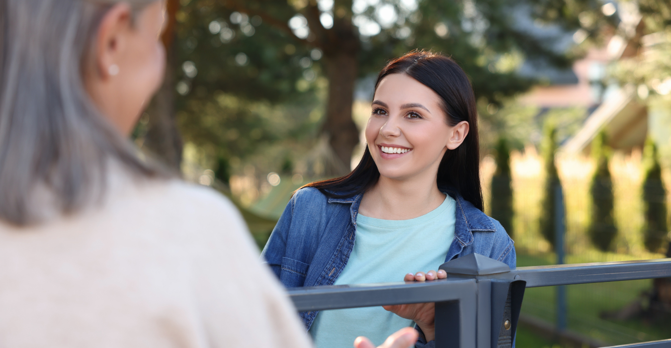 A woman smiling at a neighbour along a backyard fence.